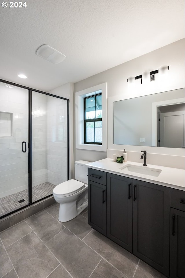 bathroom with a textured ceiling, vanity, toilet, and a shower with door