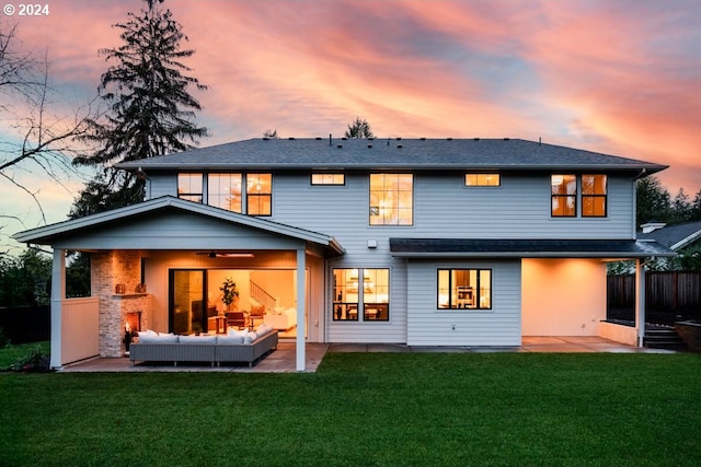 back house at dusk with outdoor lounge area, ceiling fan, a patio area, and a lawn