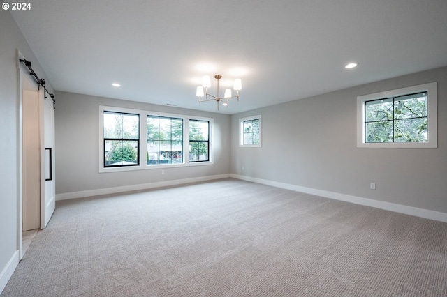unfurnished room with a barn door, a wealth of natural light, a chandelier, and light carpet