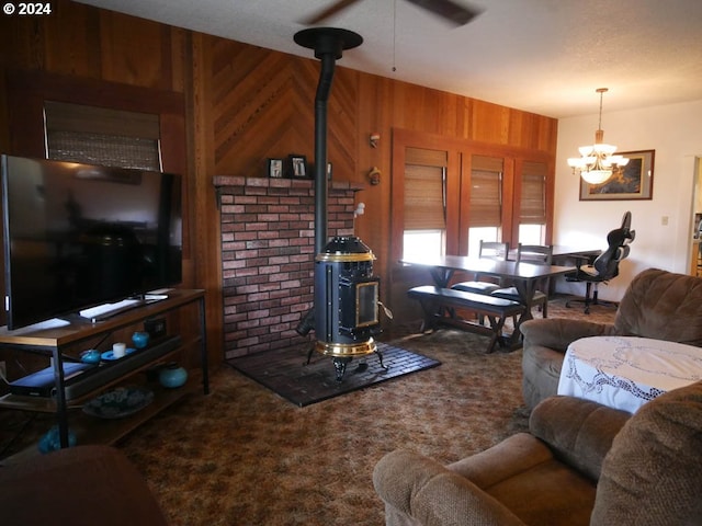 living room with carpet, ceiling fan with notable chandelier, a wood stove, and wooden walls