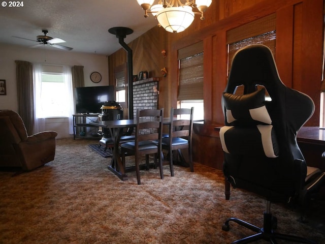 carpeted dining room with ceiling fan with notable chandelier, a textured ceiling, and wooden walls