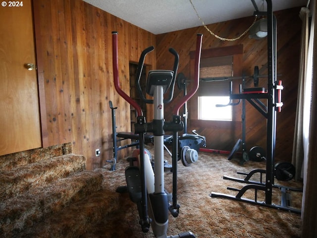 exercise room featuring carpet flooring, wooden walls, and a textured ceiling