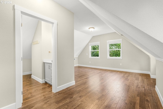 additional living space featuring hardwood / wood-style floors, lofted ceiling, and a textured ceiling