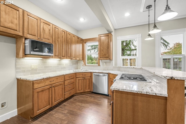 kitchen with sink, kitchen peninsula, appliances with stainless steel finishes, dark wood-type flooring, and pendant lighting