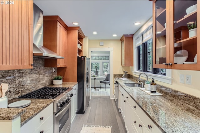 kitchen featuring appliances with stainless steel finishes, white cabinetry, light hardwood / wood-style flooring, wall chimney exhaust hood, and light stone counters