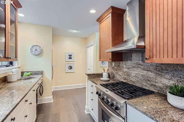 kitchen featuring wall chimney exhaust hood, high end stainless steel range oven, light stone countertops, light wood-type flooring, and white cabinetry