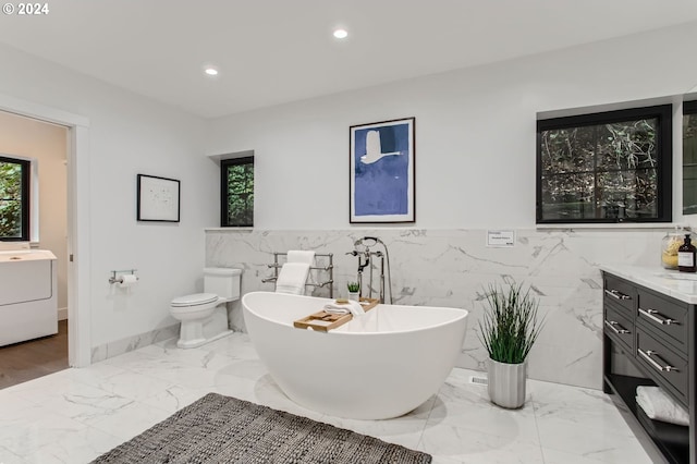 bathroom featuring a tub to relax in, toilet, a wealth of natural light, tile walls, and vanity