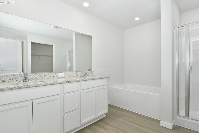 full bathroom featuring a stall shower, double vanity, a sink, and wood finished floors