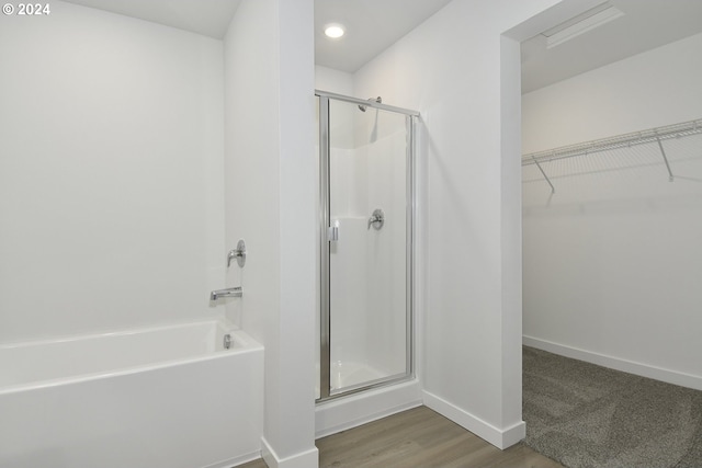 full bathroom with a washtub, wood finished floors, baseboards, a stall shower, and a walk in closet