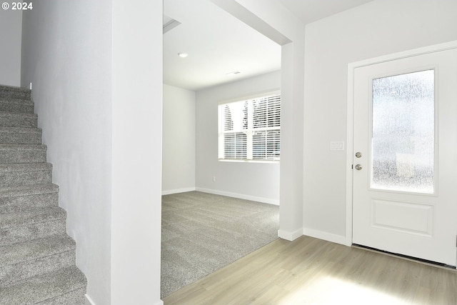 carpeted entrance foyer with stairs, baseboards, and wood finished floors