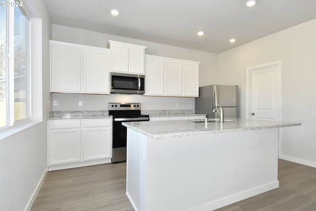 kitchen featuring appliances with stainless steel finishes, sink, light wood-type flooring, white cabinetry, and a center island with sink