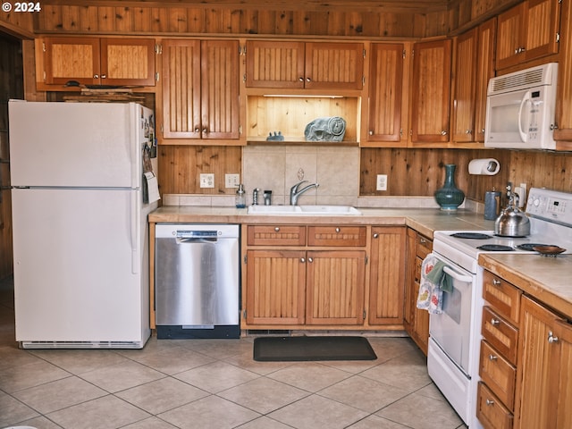 kitchen with white appliances, light tile patterned floors, sink, and wooden walls