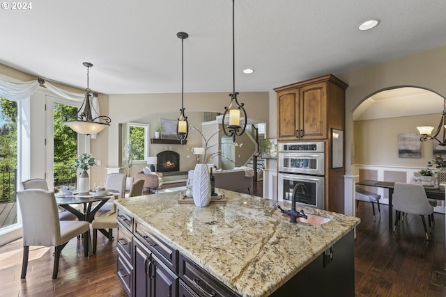 kitchen featuring dark hardwood / wood-style flooring, light stone counters, stainless steel double oven, a center island, and hanging light fixtures