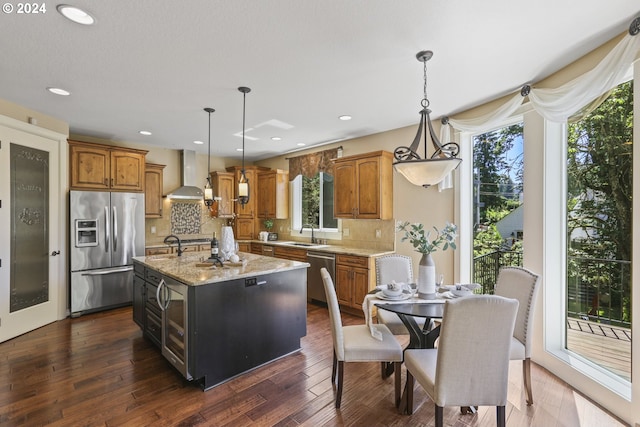 kitchen with appliances with stainless steel finishes, a center island, wall chimney exhaust hood, and pendant lighting