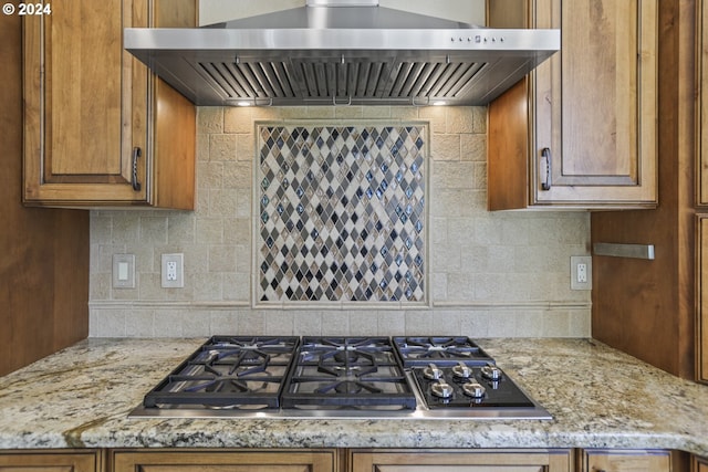 kitchen with decorative backsplash, light stone countertops, wall chimney range hood, and stainless steel gas cooktop