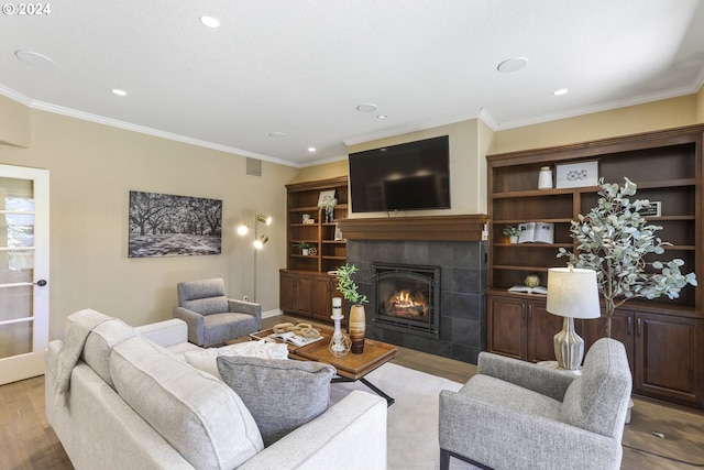 living room with crown molding, light hardwood / wood-style flooring, and a tiled fireplace