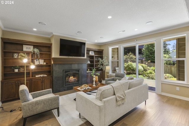 living room featuring a tiled fireplace, crown molding, a textured ceiling, and light wood-type flooring