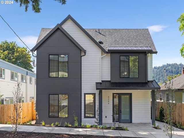 modern inspired farmhouse featuring a porch, a standing seam roof, fence, a shingled roof, and metal roof