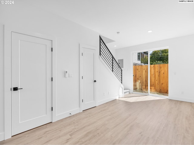 unfurnished living room with baseboards, stairway, light wood finished floors, and recessed lighting