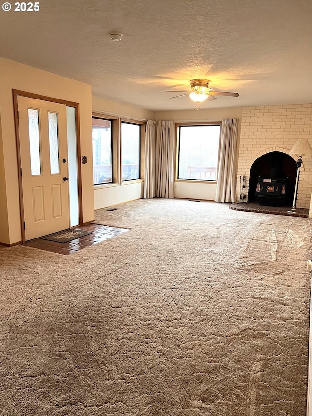 unfurnished living room featuring ceiling fan, carpet floors, a textured ceiling, and a brick fireplace