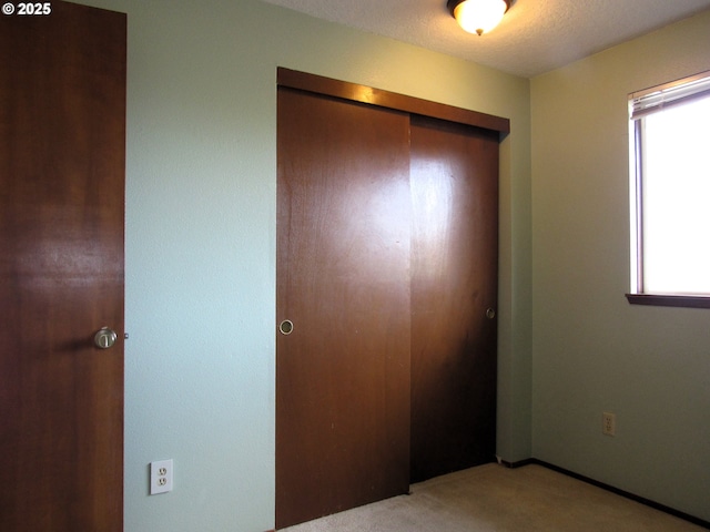 unfurnished bedroom featuring light colored carpet, a closet, and a textured ceiling