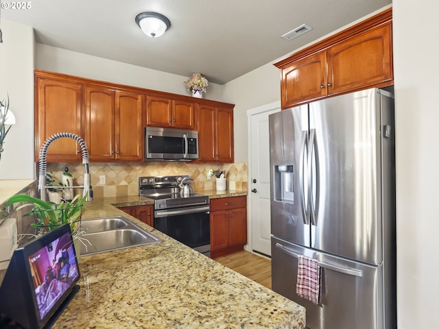 kitchen with sink, light hardwood / wood-style flooring, stainless steel appliances, light stone counters, and decorative backsplash