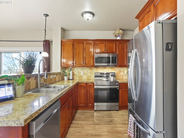 kitchen featuring a sink, appliances with stainless steel finishes, light wood finished floors, decorative light fixtures, and tasteful backsplash