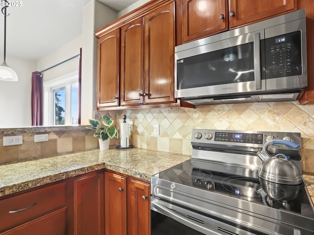 kitchen featuring stainless steel appliances, tasteful backsplash, decorative light fixtures, and light stone countertops