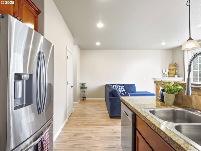 kitchen with stainless steel appliances, sink, hanging light fixtures, and light hardwood / wood-style flooring