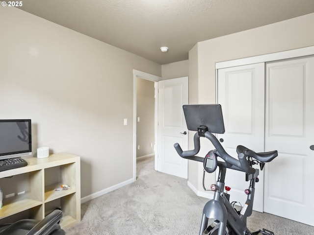 workout room featuring light carpet, baseboards, and a textured ceiling