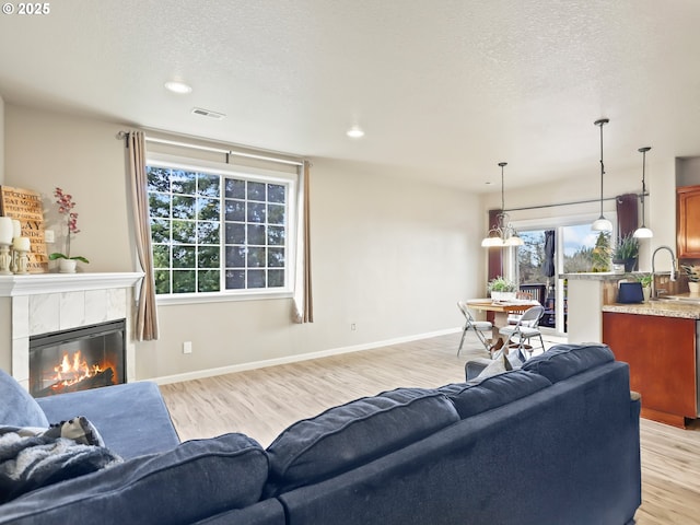 living room with a tile fireplace, sink, a textured ceiling, and light wood-type flooring