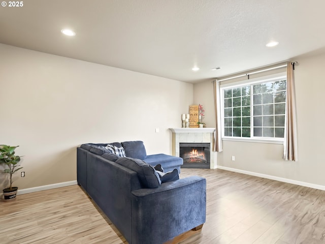 living area featuring light wood-type flooring, a tiled fireplace, baseboards, and recessed lighting