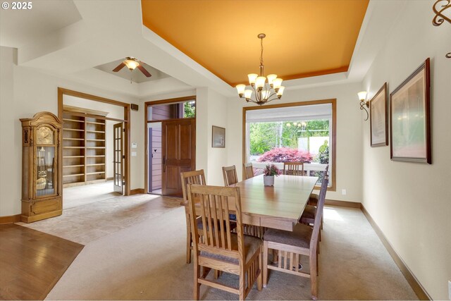 dining room with a raised ceiling, baseboards, ceiling fan with notable chandelier, and light colored carpet