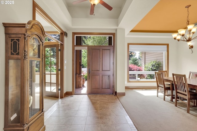 entryway with baseboards, a raised ceiling, ceiling fan with notable chandelier, and light tile patterned floors