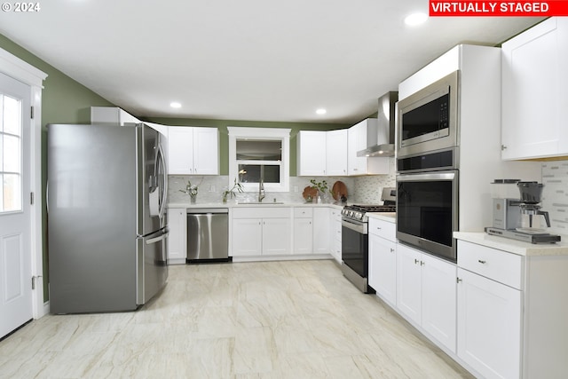 kitchen with white cabinetry, sink, wall chimney range hood, tasteful backsplash, and appliances with stainless steel finishes