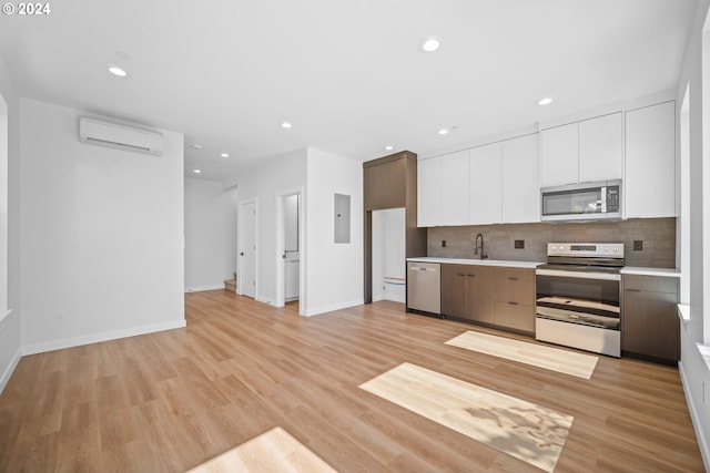 kitchen with white cabinetry, stainless steel appliances, a wall mounted air conditioner, and light wood-type flooring