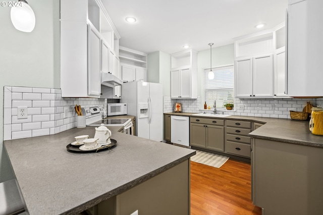 kitchen featuring kitchen peninsula, light wood-type flooring, white appliances, sink, and pendant lighting