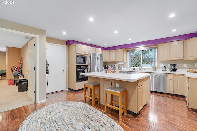 kitchen with a kitchen breakfast bar, a center island, hardwood / wood-style floors, and black appliances