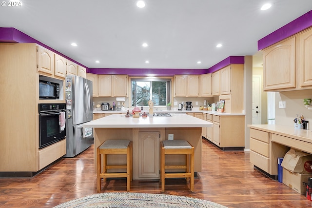 kitchen with light brown cabinets, a kitchen breakfast bar, dark hardwood / wood-style floors, a kitchen island, and black appliances