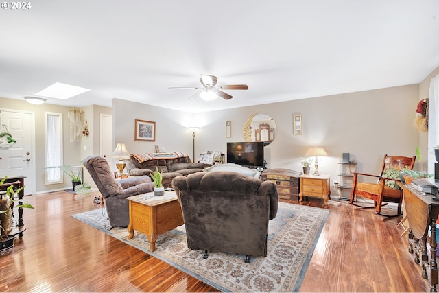 living room featuring ceiling fan, light hardwood / wood-style flooring, and a skylight