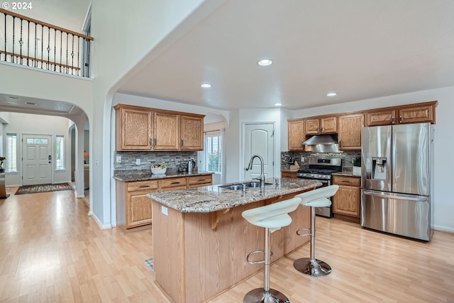 kitchen featuring stainless steel appliances, sink, stone countertops, a center island with sink, and light hardwood / wood-style floors