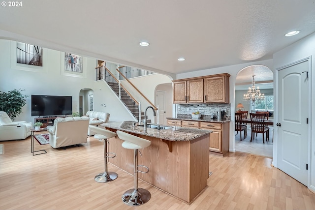 kitchen with dark stone countertops, light hardwood / wood-style flooring, a chandelier, sink, and a kitchen breakfast bar