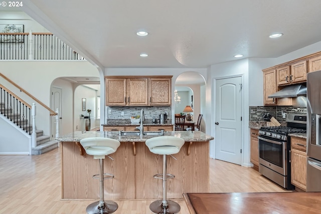 kitchen with an island with sink, stone countertops, light wood-type flooring, and gas stove