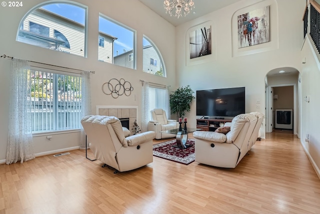 living room featuring a high ceiling, a fireplace, an inviting chandelier, and light hardwood / wood-style flooring