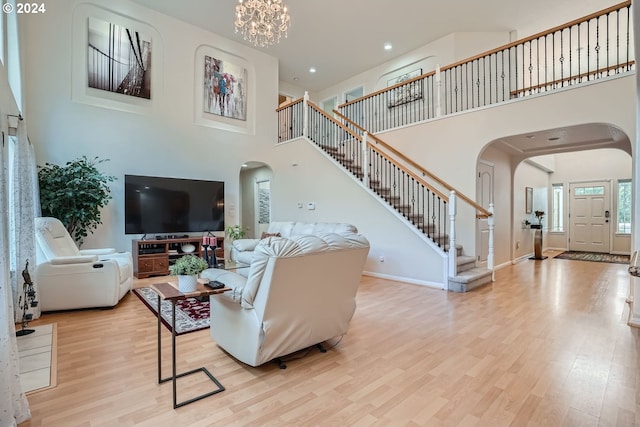 living room with light wood-type flooring, a chandelier, and a high ceiling