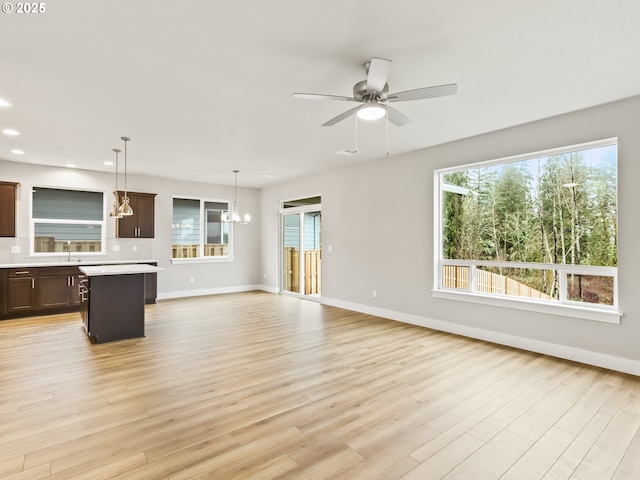 unfurnished living room featuring ceiling fan with notable chandelier and light wood-type flooring