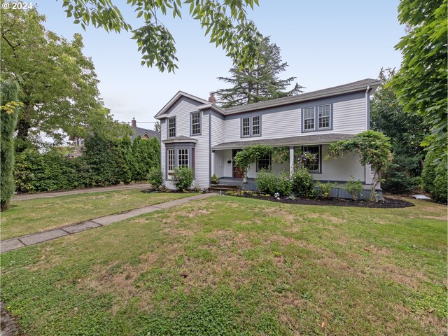 traditional-style house featuring covered porch, a chimney, and a front lawn