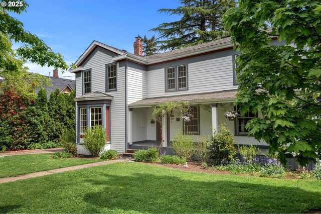 traditional-style house with covered porch, a chimney, and a front yard