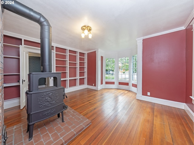 living room featuring a wood stove, crown molding, built in shelves, and hardwood / wood-style flooring