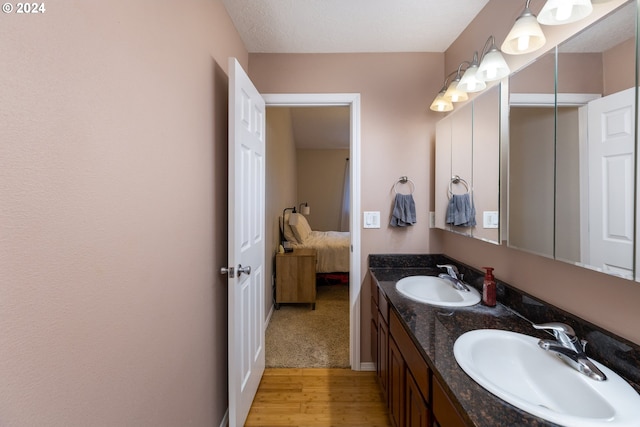 bathroom featuring wood finished floors, a sink, ensuite bathroom, and double vanity